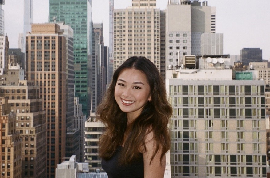 Yenli Nguyen, second-year MA student, standing in front of a view of high-rise buildings.